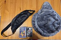 Hip sack, plush cat hammock, and two music tapes shown on wooden floor.