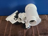 Side view showing the white plastic cylindrical pump body, inlet and outlet ports, and attached motor housing with clips.