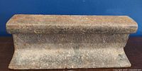 Close-up image of a solid, slightly rusted metal railway track piece placed against a blue background.