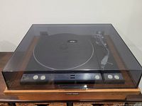 Closed record player with wood base and transparent dust cover, showing front panel with buttons and Pioneer badge.