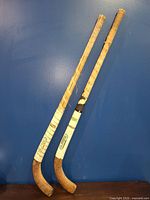 Full view of two wooden field hockey sticks with white wrapped grips showing wear and Playrite brand decals