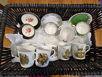 Basket containing various bone china cups, saucers, and mushroom mugs arranged on tissue paper.