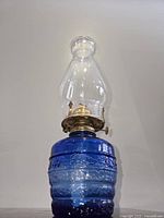 Front view of vintage cobalt blue textured glass oil lamp with clear chimney and brass burner.