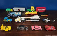 Full collection of 13 vintage toy vehicles including trucks, cars, a bus, a helicopter, and a tractor, displayed in rows on a blue background.