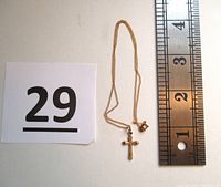Photo showing the gold cross pendant on the thin gold chain next to a ruler for size reference, pendant length about 1 inch.