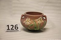 Front side view of pink Roseville pottery bowl with white irises and green leaves in relief, showing general shape and coloration.