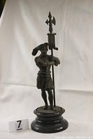 Full view of the antique French palace guard statue standing on a black round base, holding a halberd vertically.