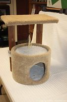 Full view of the tan and white cat tree and condo with carpeted surfaces, wooden posts, and hanging tassel toy.