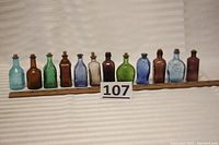 Photo showing all 12 miniature colored glass bottles arranged in a row with a measuring scale indicating about 3.25 inches each