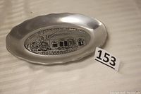 Full view of the oval scalloped pewter plate with embossed image depicting the Foundry Building and steam locomotive for Phoenixville's 150th anniversary.