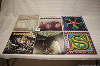 Six vinyl albums laid out on white cloth, showing front covers with various band images and colorful artwork.