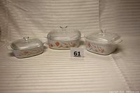 Three Corning Ware casseroles with peach floral pattern and glass lids in a group.