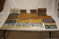 Top down view of 21 assorted vintage license plates from Pennsylvania and one New Hampshire boat plate, including cardboard temporary licenses and various vehicle types.