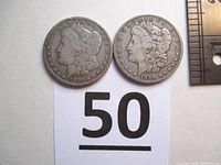 Photo of both 1886 and 1896 Morgan silver dollars side by side, showing obverse images with Lady Liberty and dates visible.