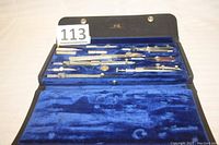 Open black case lined in blue velvet holding 11 drafting tools including compasses and dividers, with 'K&E' logo visible on case interior.