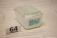 Vintage white opaque Pyrex storage dish with teal Amish Butterprint depicting rooster and corn stalks, clear lid on top.