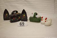 Overall view showing vintage ceramic chicken shakers in a green basket, black clothing iron shaped shakers with floral designs and matching box, plus two Westmoreland milk glass hen shaped salt cellars.