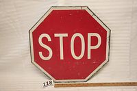 Front view of vintage steel STOP sign, octagonal shape, red background and white text with scrapes and marks.