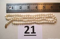 Full view of the white pearl necklace laid next to a ruler showing length approximately 25 inches. Pearls are uniform and knotted individually.