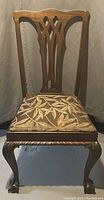 Front view of a wooden accent chair showing carved backrest and leaf patterned upholstered seat.