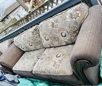 Photo of the couch showing floral cushions with beige, gold, and brown tones, brown textured fabric on arms and base, wooden accent on armrest