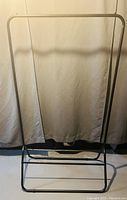Clothes trolley metal frame against curtain backdrop showing full structure including base and hanging bar.