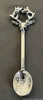 Photo showing one silver-colored collectable spoon with a detailed deer head and antlers on the handle and a textured spoon bowl.