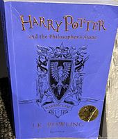 Photo of the front cover of the Harry Potter and the Philosopher's Stone Ravenclaw edition hardcover book with embossed gold title and Ravenclaw crest.