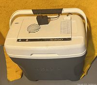 Top and slightly angled view of the Igloo electric cooler showing ventilation grills, control buttons, and attached power adapter on the lid.