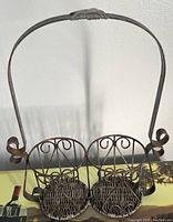 Photo of metal condiment set consisting of two woven baskets held in a metal stand with a large curved handle and scroll sides.