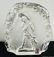 Front view of clear glass sculpture showing raised soldier figure and textured edges.