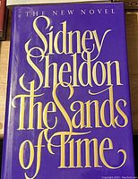 Front cover of Sidney Sheldon's novel 'The Sands of Time' showing purple cover with gold large script lettering.