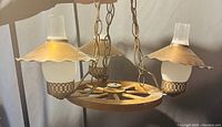 Vintage ceiling light fixture resembling a wooden wagon wheel with three brass and frosted glass light fixtures hanging from it, suspended by brass chains.