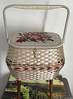 Front and side view of the vintage woven footed sewing box with embroidered floral lid from Eaton's, showing legs and the latch