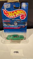 Photo showing front and side view of green die-cast 1965 Chevrolet Impala in original Hot Wheels packaging