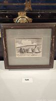 Framed nautical art print showing sailboats on water with buildings and hills behind. Frame shows wear.