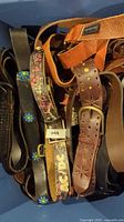 Overhead view of multiple brown and black leather belts in bin, assorted buckle styles and leather textures visible.