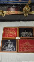 Four metal plaques mounted on wood, displayed in two rows, each plaque showing CNE landmarks with engraved metal art and text.