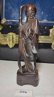 Front view of the wooden sculpture showing Shao Lao standing with staff and detailed facial features.