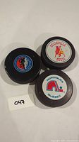 Top view of all three hockey pucks showing Quebec Nordiques, Belleville Bulls, and Hockey Hall of Fame logos.