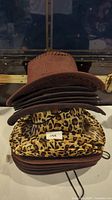 Stack of brown suede style cowboy hats with ventilation holes and leopard print cowboy hats below.