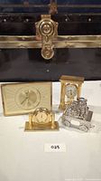 Four vintage items on white surface: Sabre Regency clock, gold-tone miniature clock, carriage-style clock, and silver-tone cart collectible.