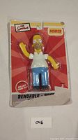 Front view of Homer Simpson bendable figure in blister packaging, showing some wear and tear at the bottom of the cardboard backing.