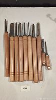 Set of 10 woodworking carving tools laid out on a surface, showing full length of tools with wooden handles and metal blades.