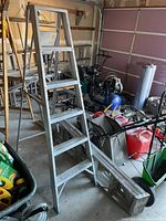 Side view of taller aluminum step ladder showing five steps and spreader support in a cluttered garage.