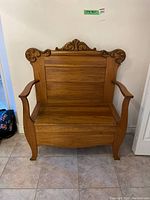 Front view of the wooden bench showing the high back with decorative carved details, armrests, and seat that lifts for storage.