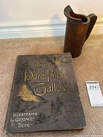 Full view of the book 'The Doré Bible Gallery' with wooden pitcher beside it on carpeted floor.