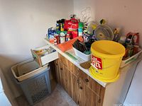 Overview of cleaning products, small yellow bucket, fan, and other items arranged on a cabinet.