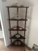 Front view of the entire corner shelf showing all five tiers with various decorative plates and items placed for display only (contents not included).