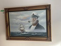 Framed canvas art hung on a wall showing a bearded sailor and sailing ship on sea, signed by P. Martyns.